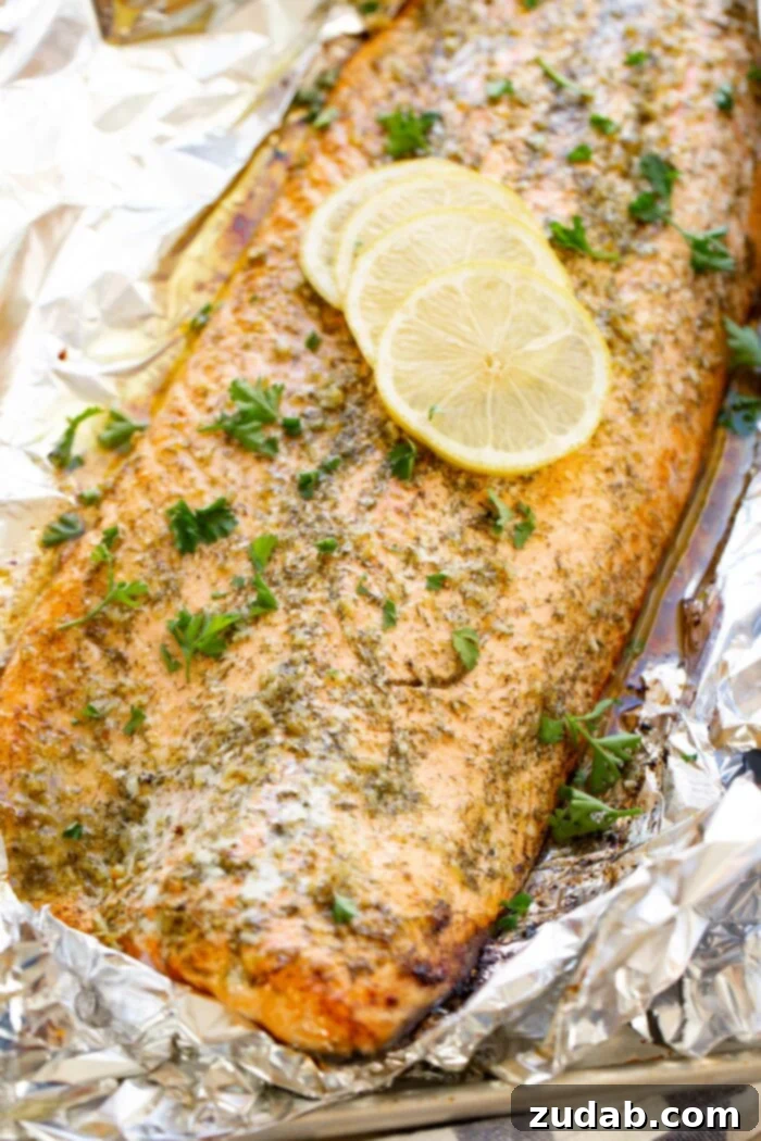 Perfect Garlic Butter Salmon 2 A photo of a baked salmon filet sitting in aluminum foil garnished with fresh parsley and for lemon slices