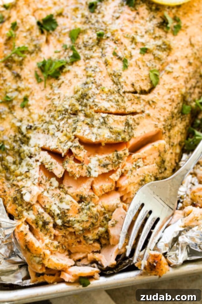 Perfect Garlic Butter Salmon 3 A photo of a baked salmon filet flaked with a fork, garnished with fresh parsley, and sitting on a foil and