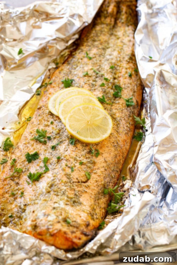 Perfect Garlic Butter Salmon 4 A photo of a baked salmon filet sitting in aluminum foil garnished with fresh parsley and four lemon slices