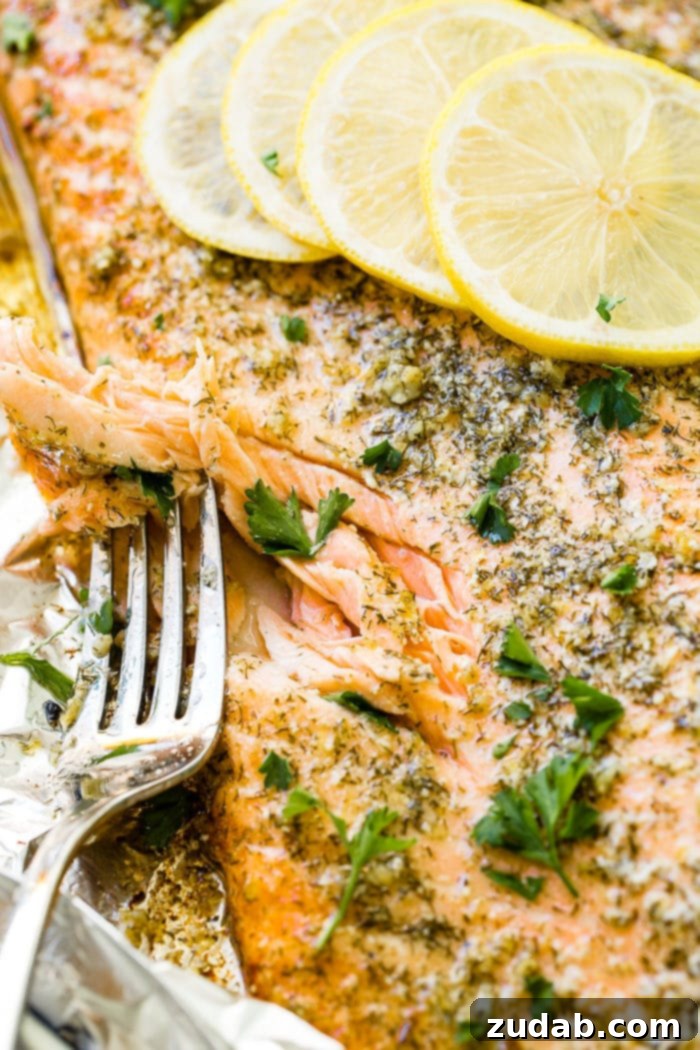 Perfect Garlic Butter Salmon 5 A photo of a baked salmon filet flaked with a fork, garnished with dill and fresh parsley, and sitting on aluminum foil