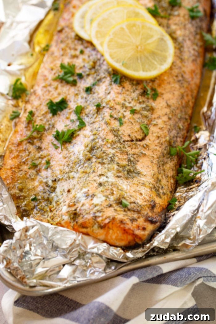 Perfect Garlic Butter Salmon 7 A photo of a baked salmon filet sitting in aluminum foil garnished with fresh parsley and four lemon slices