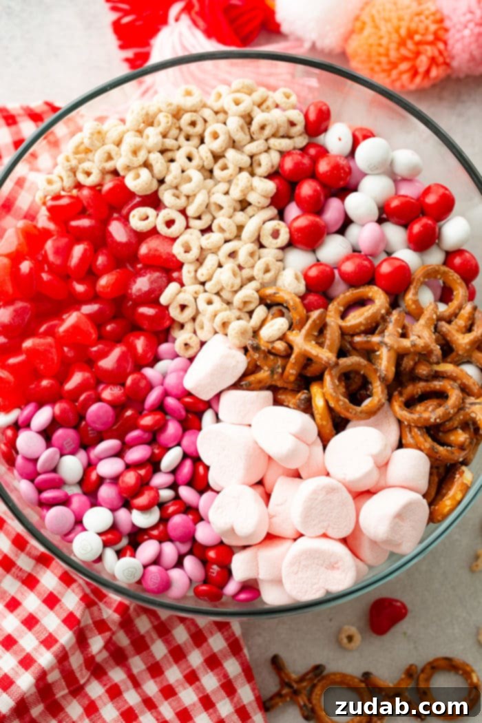 5-Minute Valentine's Treat Mix 2 A photo of a large glass bowl full of frosted cheerios, Valentine's caramel M&Ms, X and O shaped pretzels, pink heart marshmallows, Valentine's colored plain M&Ms, and heart shaped Starburst jelly beans, ready to be enjoyed as a festive Valentine's Day treat.