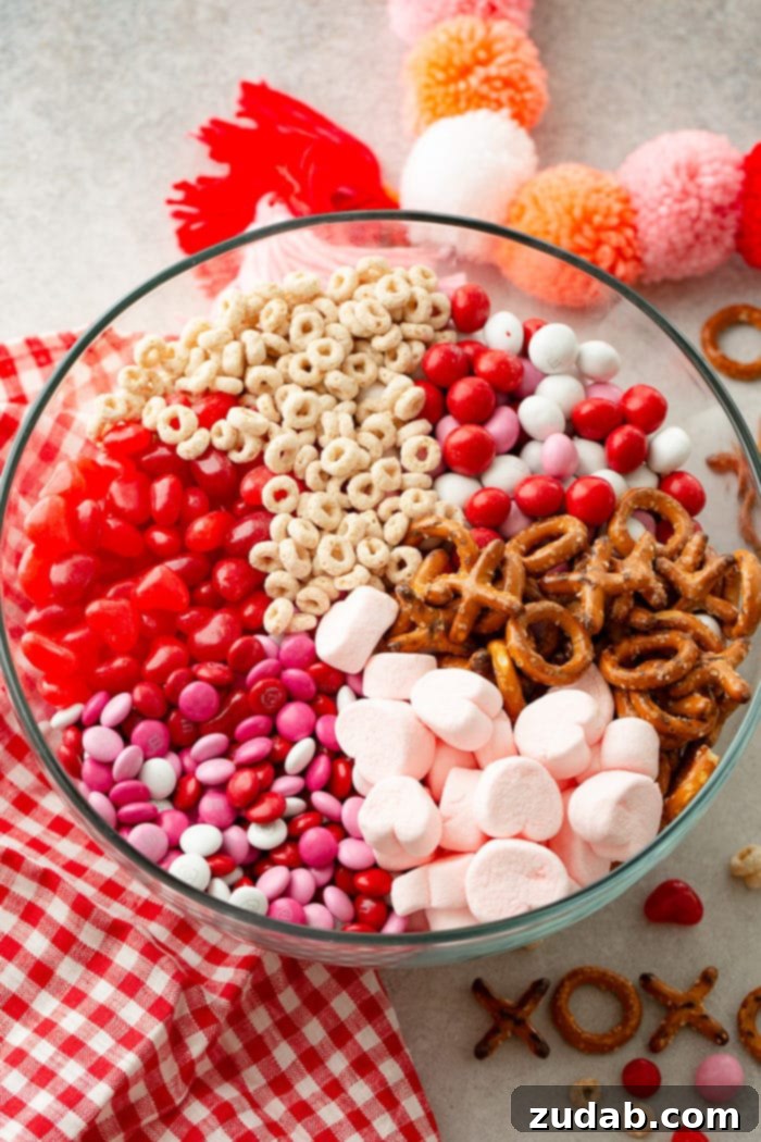 5-Minute Valentine's Treat Mix 4 A beautiful shot of a large glass bowl overflowing with a festive Valentine's snack mix, featuring Frosted Cheerios, colorful M&Ms, playful X and O pretzels, sweet heart-shaped marshmallows, and tangy Starburst jelly beans, perfect for sharing.