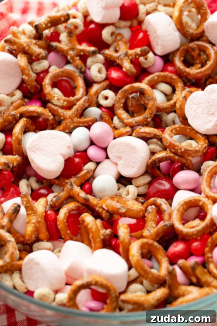 5-Minute Valentine's Treat Mix 5 A vibrant close-up photograph of a Valentine's snack mix, showcasing the delightful combination of frosted cheerios, Valentine's caramel M&Ms, X and O shaped pretzels, soft pink heart marshmallows, classic Valentine's colored plain M&Ms, and chewy heart-shaped Starburst jelly beans, highlighting their varied textures and festive colors.