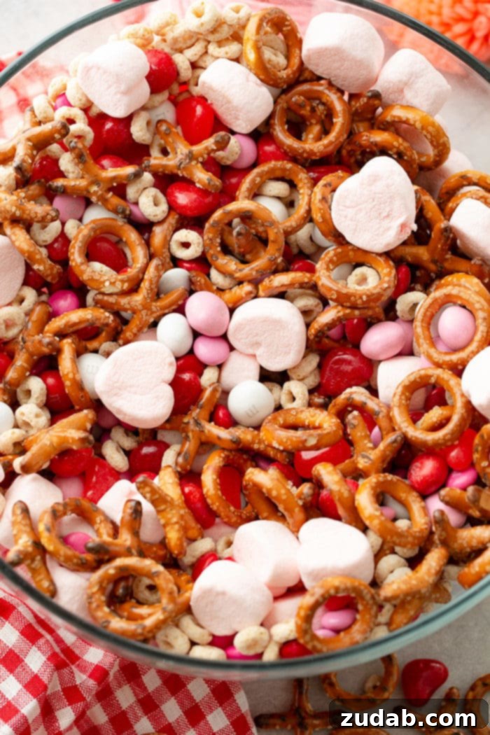 5-Minute Valentine's Treat Mix 7 A delightful close-up of a Valentine's snack mix, featuring a vibrant blend of frosted cheerios, Valentine's caramel M&Ms, playful X and O pretzels, soft pink heart marshmallows, classic Valentine's colored plain M&Ms, and chewy heart-shaped Starburst jelly beans.