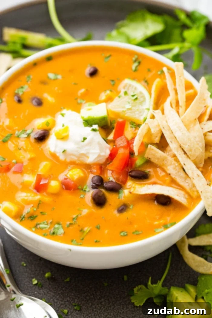 My Ultimate Chicken Tortilla Soup Recipe 4 A close-up photo of a white bowl of homemade chicken tortilla soup, richly garnished with a dollop of sour cream, a bright lime wedge, and an abundance of crunchy tortilla strips.