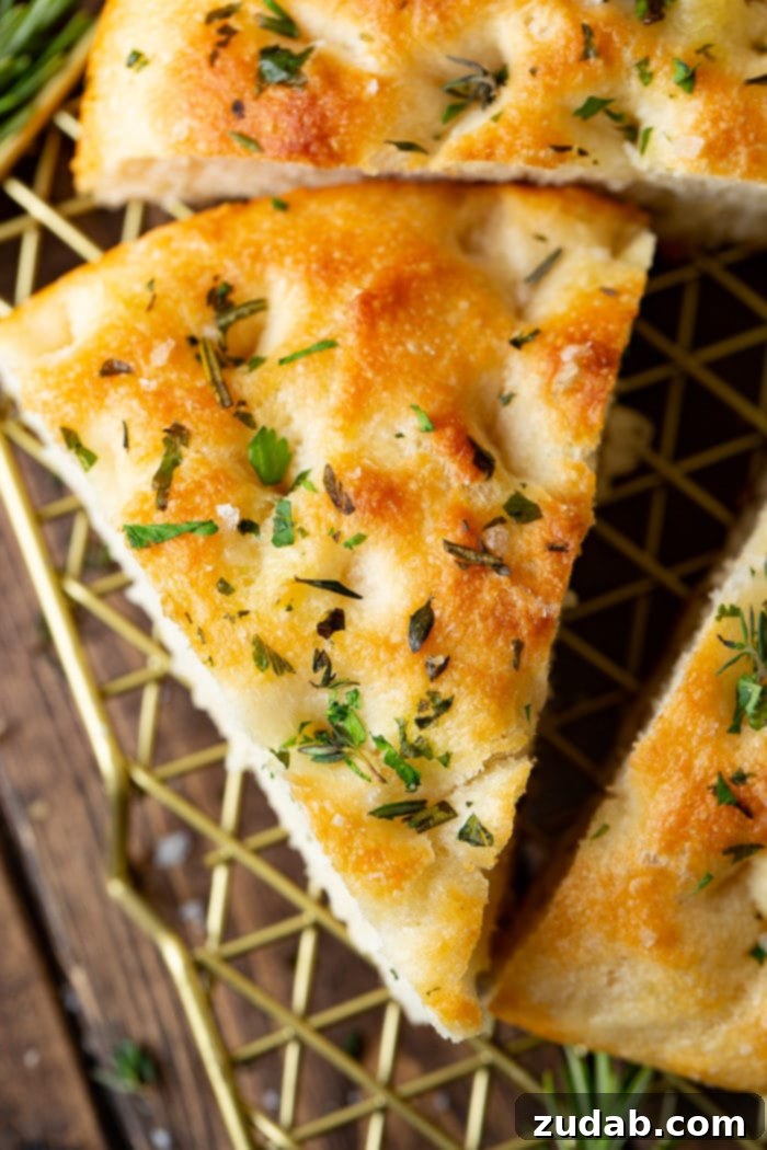 Effortless Aromatic Focaccia Bread 4 A photo of a triangular slice of golden focaccia bread, showcasing its airy texture, fresh green herbs, and visible salt flakes on top. The crust is beautifully golden-brown and crisp.