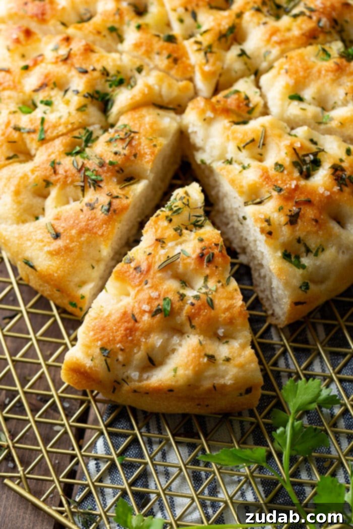 Effortless Aromatic Focaccia Bread 6 A beautifully baked round focaccia bread loaf, generously topped with fresh herbs and sea salt, with a wedge already cut out and positioned alongside the main loaf, ready to be enjoyed.
