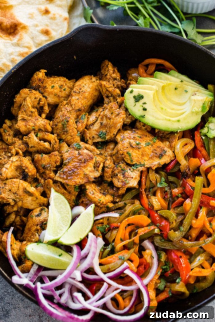 Family-Friendly One-Skillet Chicken Fajitas 2 A photo of a cast iron skillet full of chicken fajita filling - cooked chicken, sauteed peppers and onions, lime wedges, sliced purple onion, and sliced avocados.