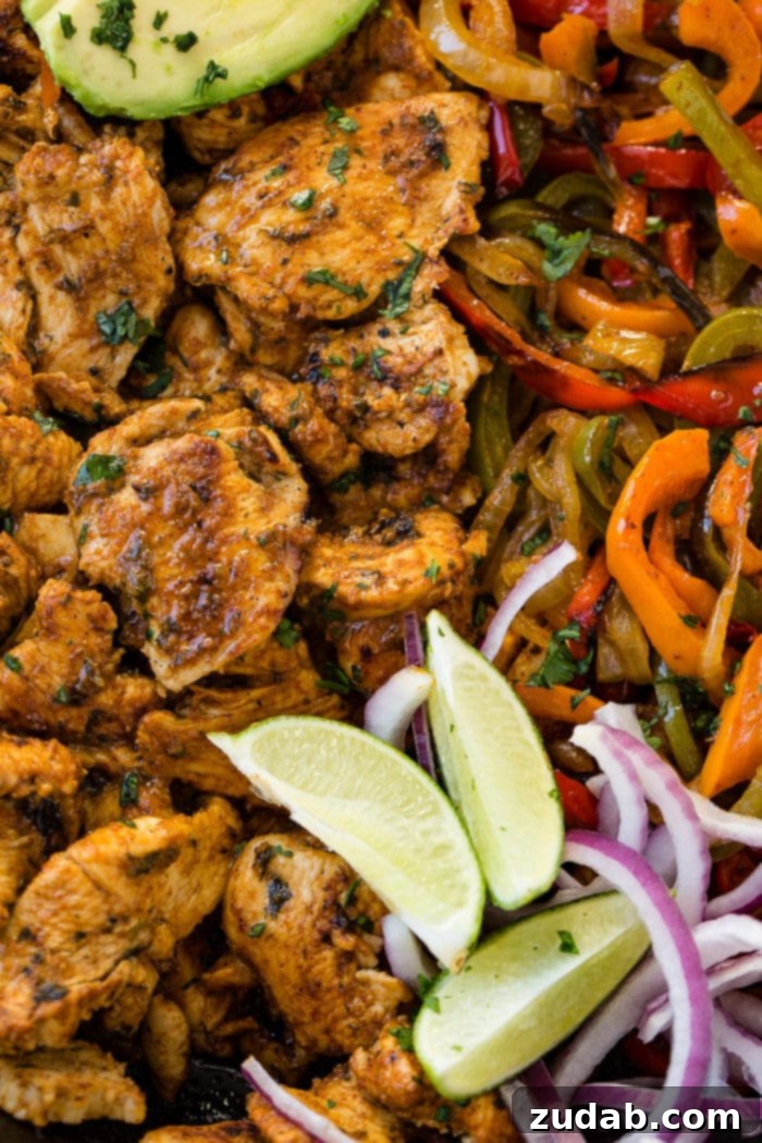 Family-Friendly One-Skillet Chicken Fajitas 3 A closeup photo ofchicken fajita filling - cooked chicken, sauteed peppers and onions, lime wedges, sliced purple onion, and sliced avocados.