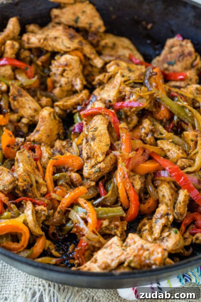 Family-Friendly One-Skillet Chicken Fajitas 6 A photo of a cast iron skillet full of chicken fajita filling - cooked chicken and sauteed peppers and onions