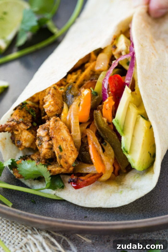 Family-Friendly One-Skillet Chicken Fajitas 8 A photo of a flour tortilla filled with chicken fajita filling, sliced red onions, and sliced avocadoes.