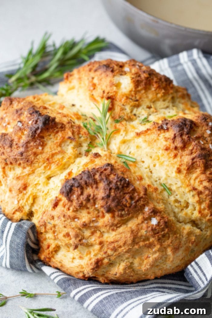 Garlic Cheddar Herb Irish Soda Bread 2 A whole loaf of garlic cheddar herb irish soda bread sitting on a blue and white striped cloth napkin and topped with sprigs of fresh rosemary