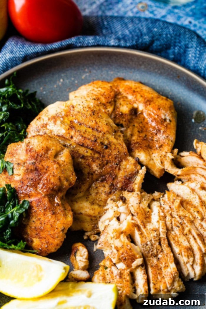 Juicy Traeger Smoked Chicken Breast, Effortlessly 2 A photo of whole smoked chicken breasts and sliced smoked chicken breasts on a charcoal gray plate with lemon wedges and kale on the side.