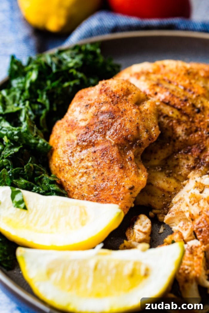 Juicy Traeger Smoked Chicken Breast, Effortlessly 3 A photo of whole smoked chicken breasts and on a charcoal gray plate with lemon wedges and kale on the side.