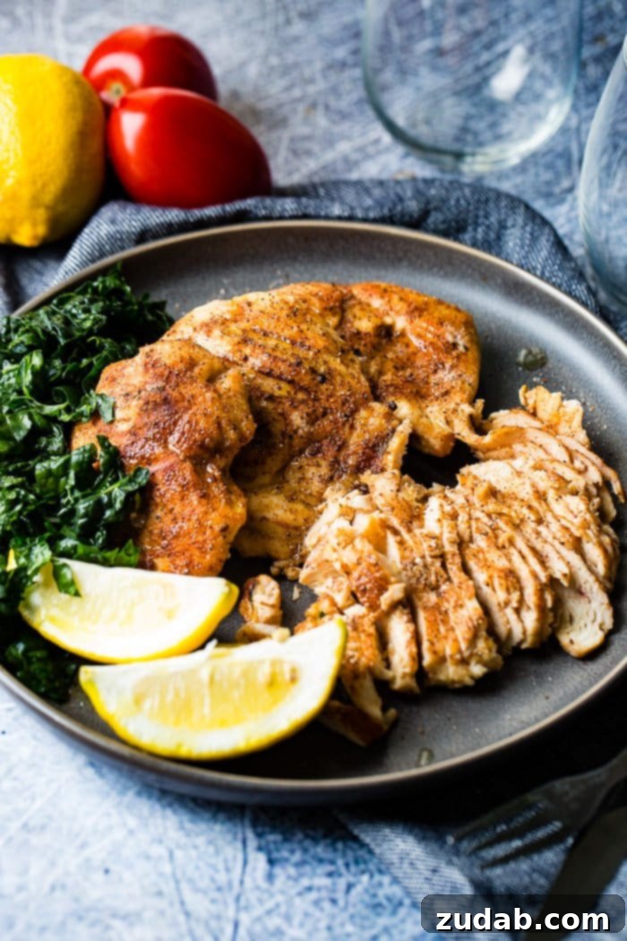 Juicy Traeger Smoked Chicken Breast, Effortlessly 4 A photo of whole smoked chicken breasts and sliced smoked chicken breasts on a charcoal gray plate with lemon wedges and kale on the side.