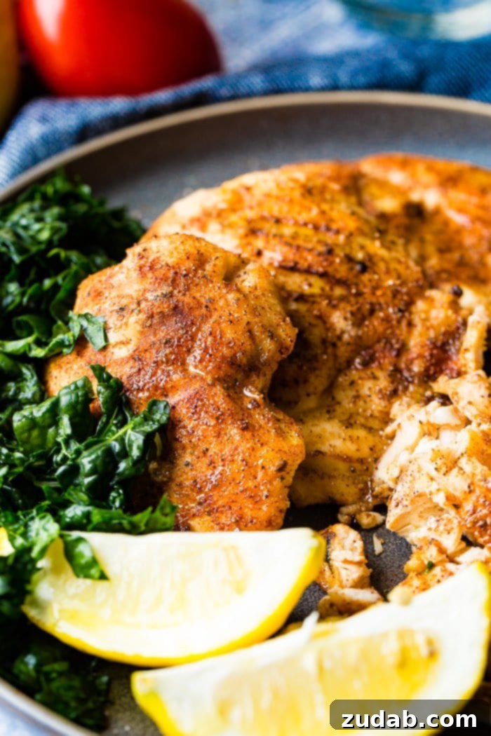Juicy Traeger Smoked Chicken Breast, Effortlessly 6 A photo of whole smoked chicken breasts and sliced smoked chicken breasts on a charcoal gray plate with lemon wedges and kale on the side.