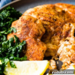 Juicy Traeger Smoked Chicken Breast, Effortlessly 7 A photo of whole smoked chicken breasts and sliced smoked chicken breasts on a charcoal gray plate with lemon wedges and kale on the side.