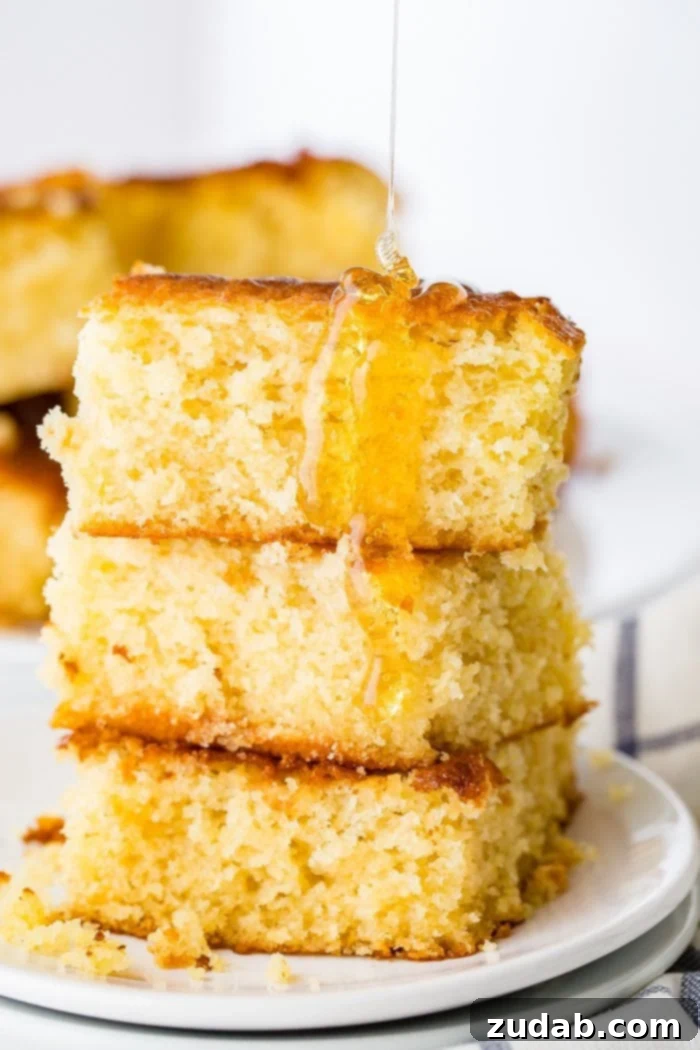The Ultimate Moist and Sweet Cornbread Recipe with Video 5 A beautiful photo displaying three pieces of homemade cornbread, stacked invitingly, with golden honey generously drizzled all over them.