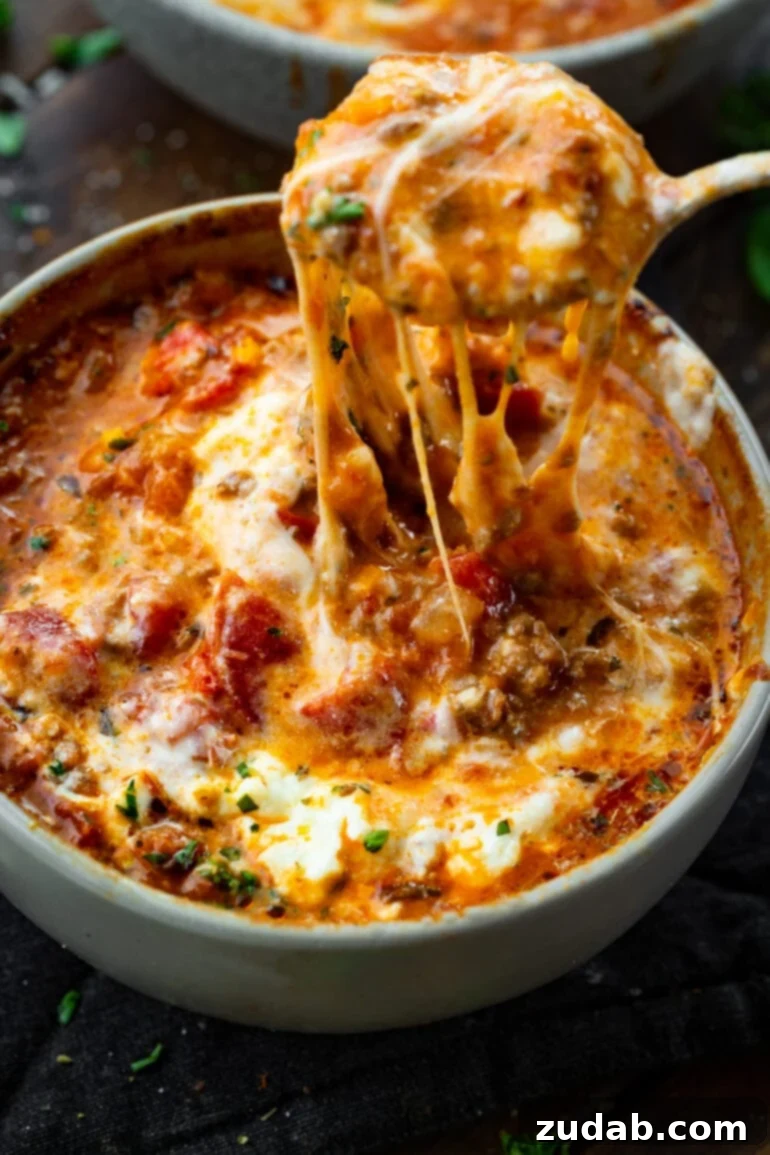 Delicious Lasagna Soup Recipe 2 A steaming bowl of lasagna soup, generously topped with melted cheese, with a spoon lifting a cheesy, pasta-filled bite.