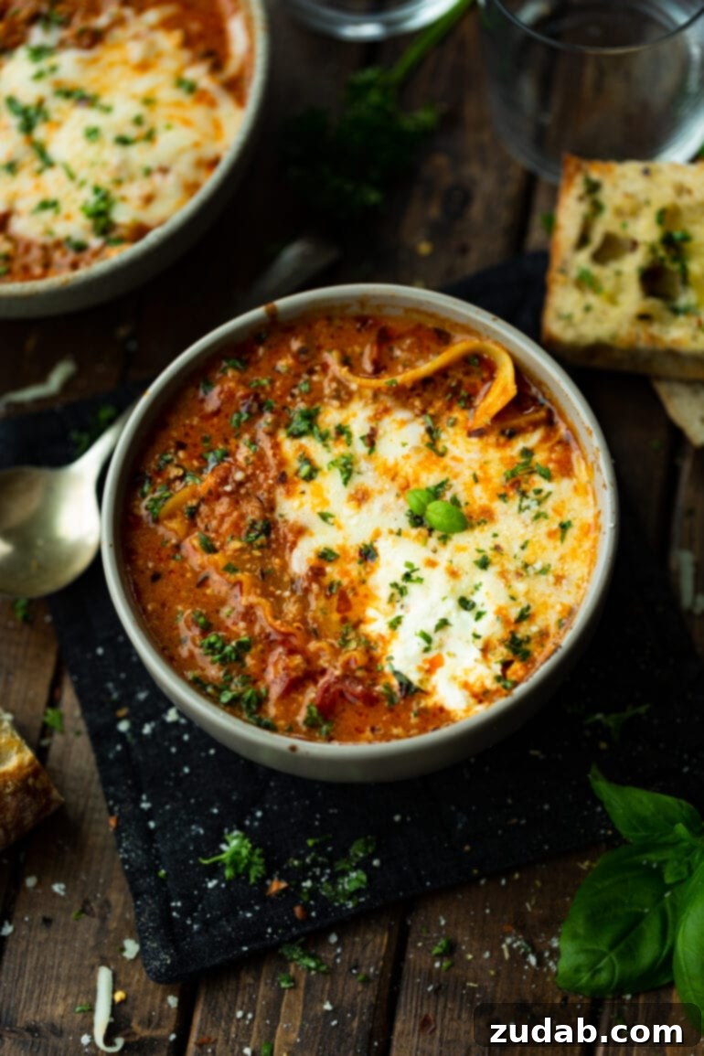 Delicious Lasagna Soup Recipe 5 A pristine white soup bowl overflowing with hearty lasagna soup, beautifully crowned with a generous layer of melted mozzarella cheese.