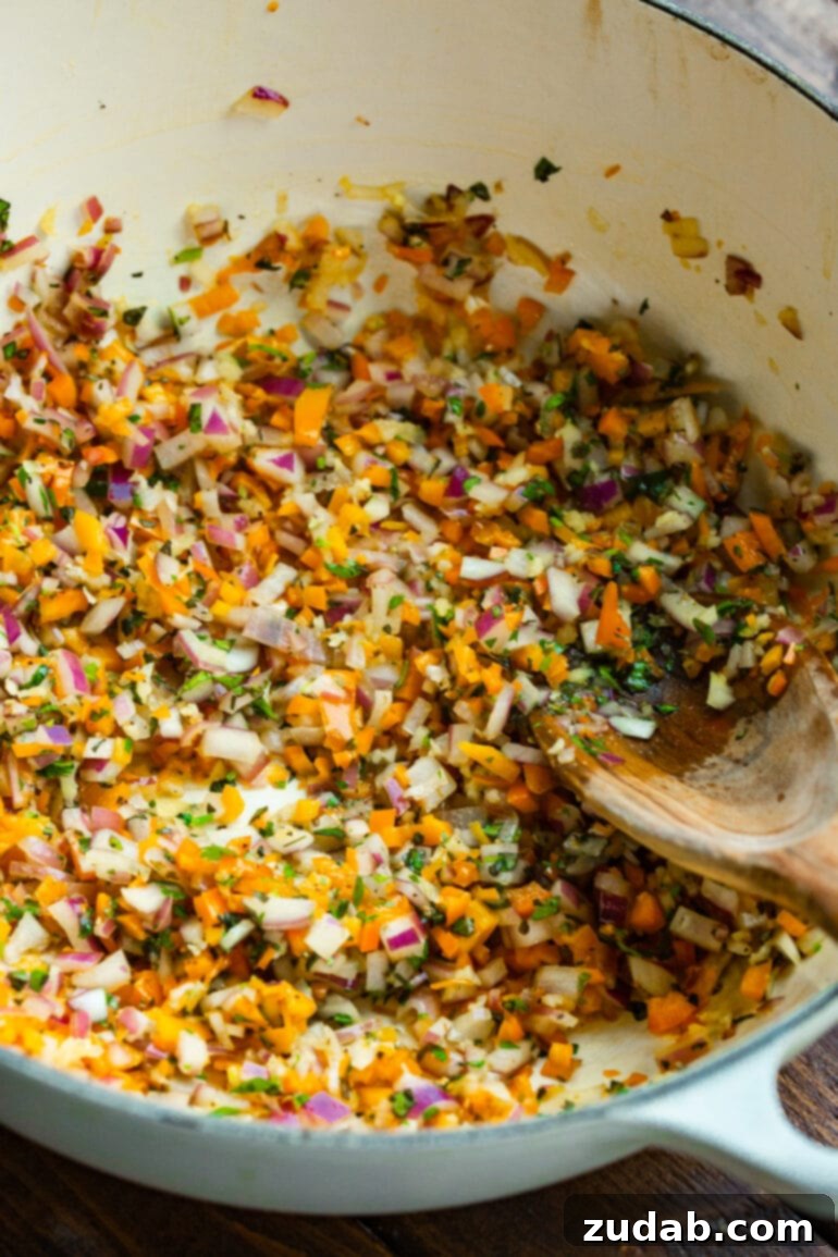 Delicious Lasagna Soup Recipe 6 A close-up photo of minced red onions, garlic, colorful bell pepper, and fresh herbs being sautéed in a ceramic Dutch oven.