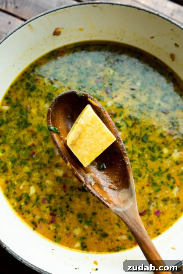 Delicious Lasagna Soup Recipe 8 A small section of Parmesan rind resting on a wooden spoon, held above a simmering pot of rich lasagna soup.