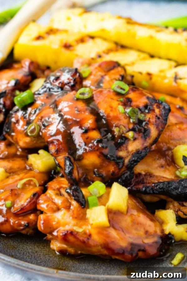 Easy Huli Huli Grilled Chicken Video Guide 2 A photo of grilled huli huli chicken with grilled pineapple in the background.