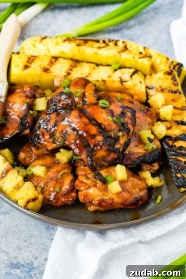 Easy Huli Huli Grilled Chicken Video Guide 3 A photo of grilled huli huli chicken with grilled pineapple in the background.