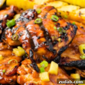 A photo of grilled huli huli chicken with grilled pineapple in the background.