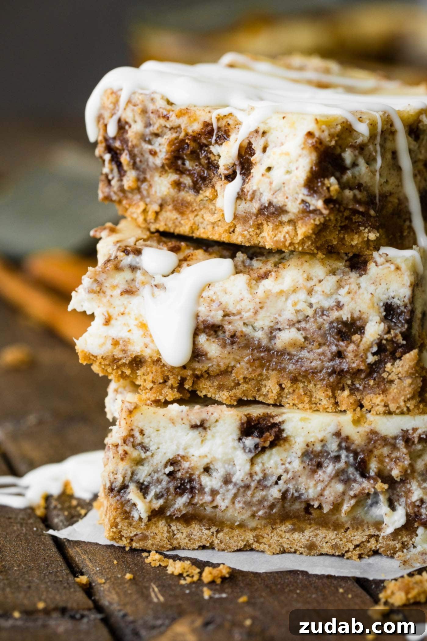 Blender Cinnamon Roll Cheesecake Bars A photo of three cinnamon roll cheesecake bars stacked on top of each other, showcasing the cinnamon swirl.