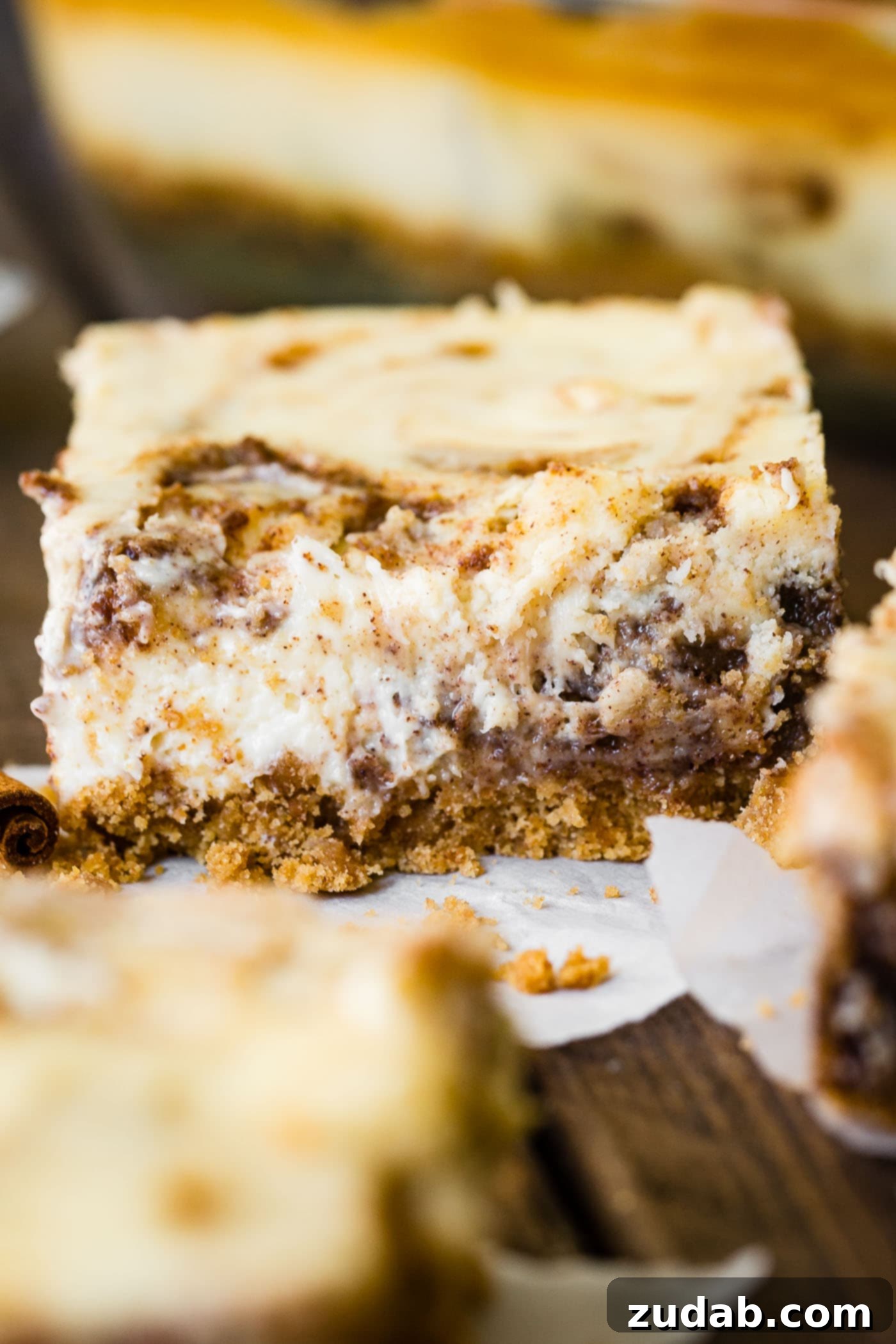 Blender Cinnamon Roll Cheesecake Bars A close-up photo of a single cinnamon roll cheesecake bar, showing the creamy texture and cinnamon swirl.
