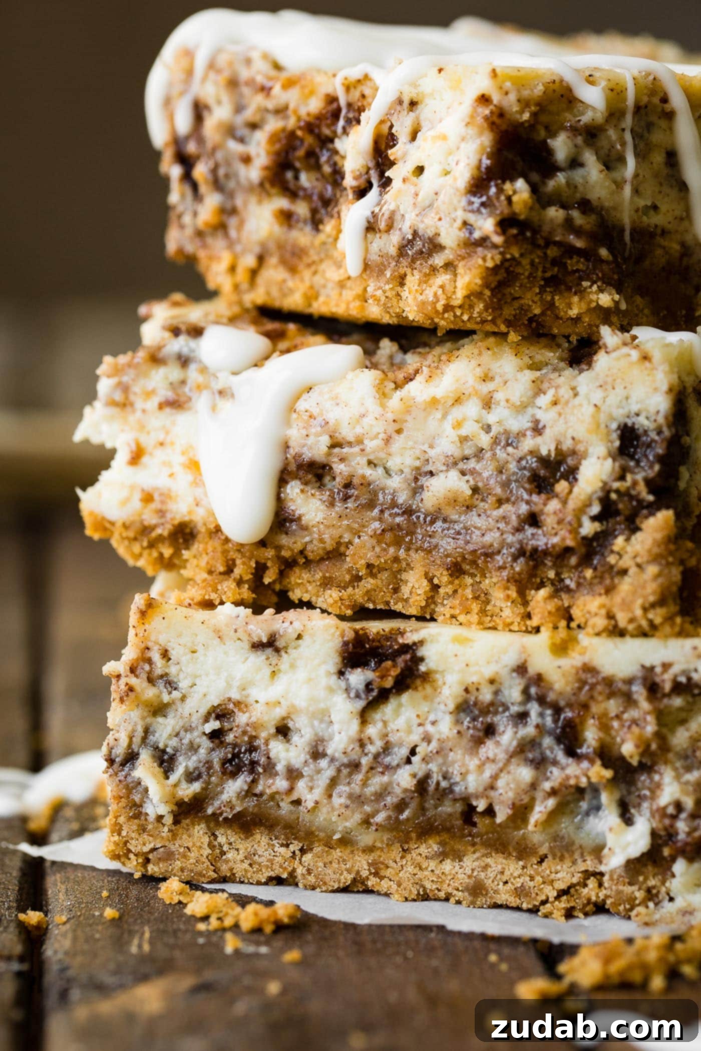 Blender Cinnamon Roll Cheesecake Bars A photo of three cinnamon roll cheesecake bars stacked on top of each other, showing the delightful layers.
