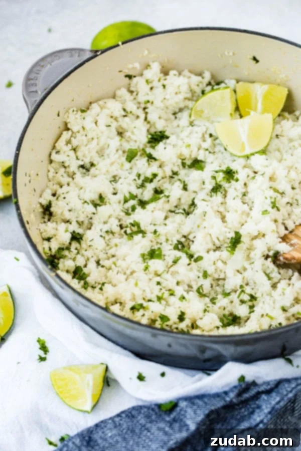 Zesty Cilantro Lime Cauliflower Rice 2 A close-up photo of a pot of cilantro lime cauliflower rice, garnished with fresh lime wedges and a wooden spoon, showcasing its vibrant texture.