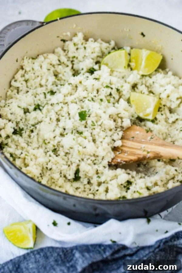 Nutrient-Rich Cilantro Lime Cauliflower Rice A photo of a pot full of cilantro lime cauliflower rice with fresh lime wedges sitting on top and a wooden spoon in it, inviting diners to enjoy.