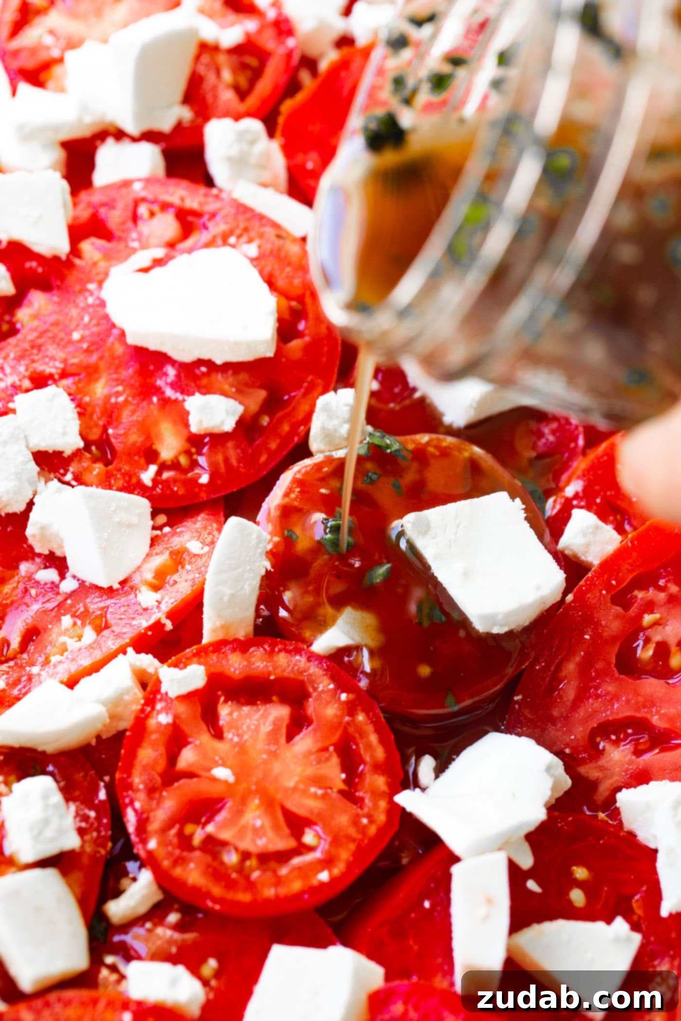 3 Cheese Marinated Tomatoes Salad A hand pouring glossy balsamic vinegar dressing over a colorful array of sliced tomatoes, ready to be transformed into a marinated salad.
