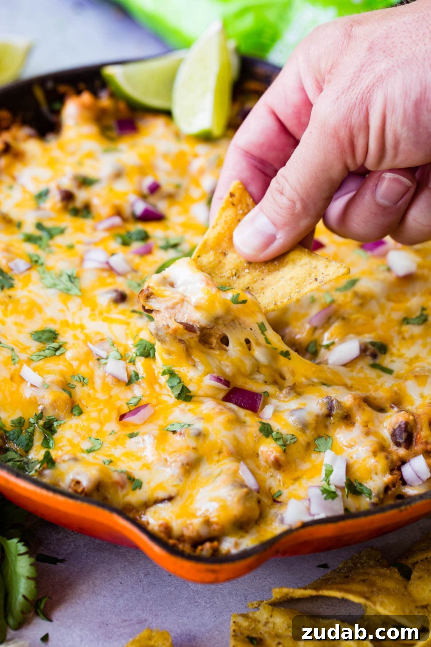 Easy One Skillet Cheesy Black Bean Dip A photo of someone scooping black bean dip out of a skillet with a tortilla chip.