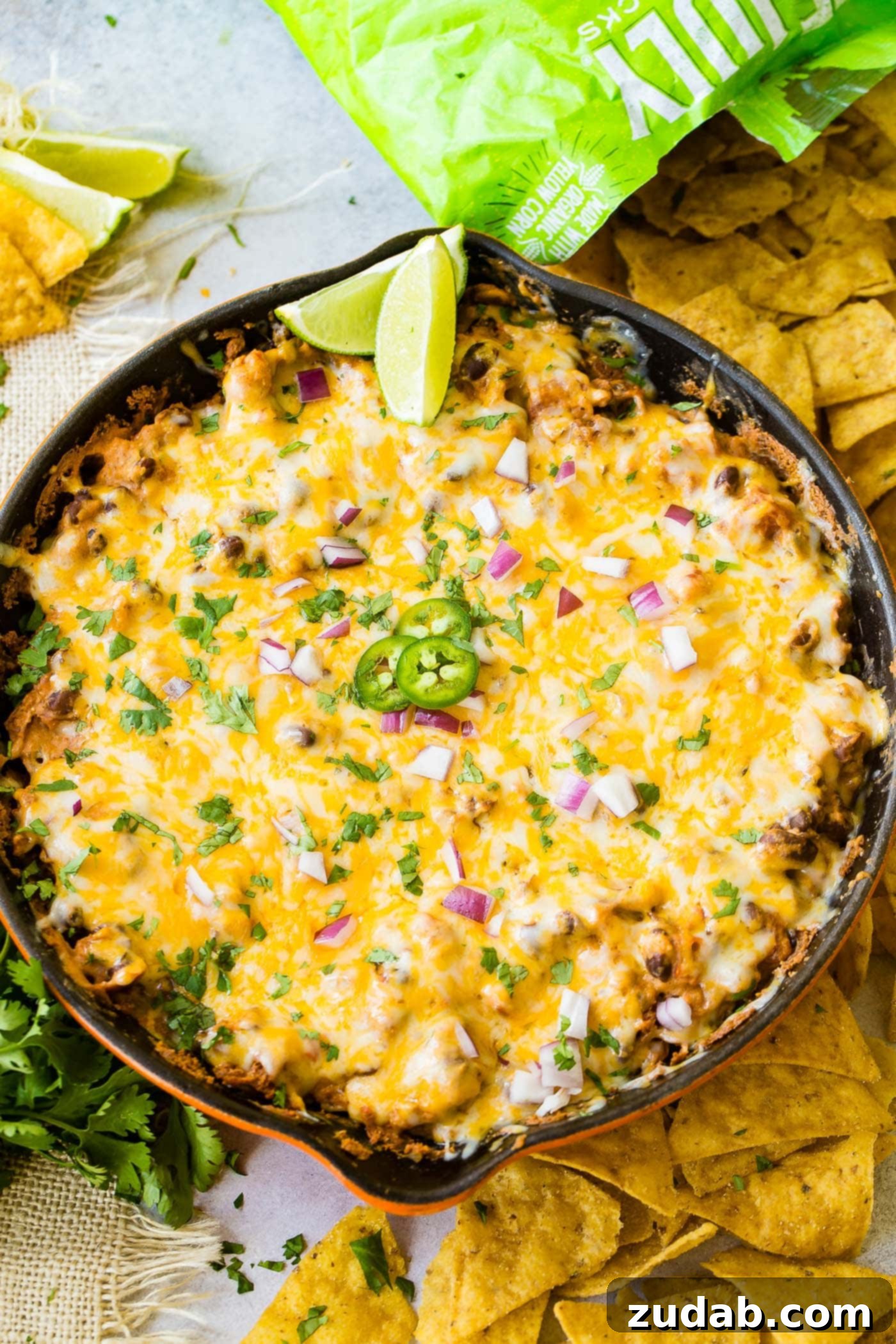 Easy One Skillet Cheesy Black Bean Dip A photo of a cast iron skillet full of black bean dip covered in melted cheese and topped with diced red onion, fresh cilantro, sliced jalapenos and lime wedges.
