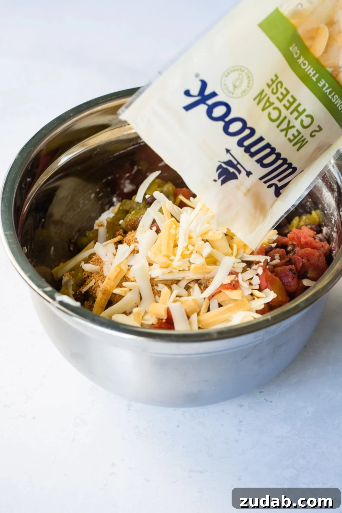Easy One Skillet Cheesy Black Bean Dip A photo of Tillamook Mexican 2 Cheese blend being added to a bowl of ingredients for black bean dip.