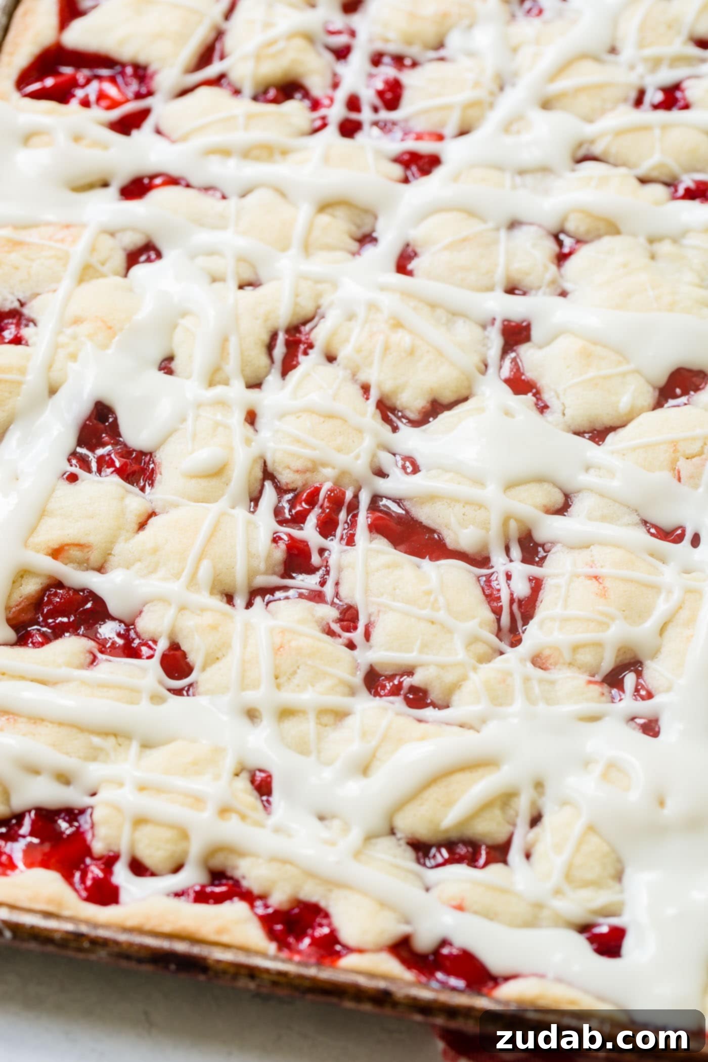 Sweet Cherry Sugar Cookie Bars 6 A cookie sheet pan filled with golden cherry pie bars, generously drizzled with a sweet white glaze.