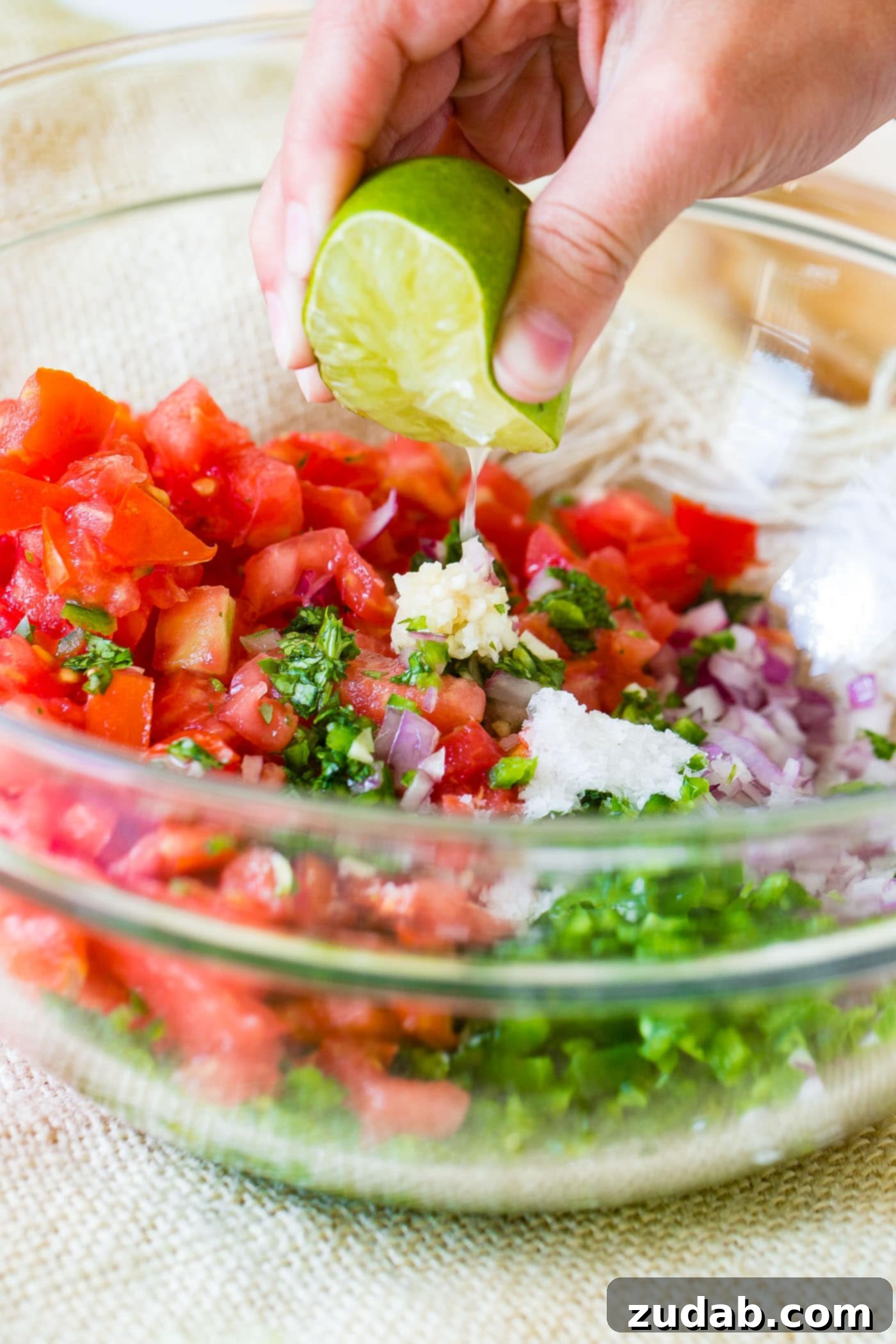 Fresh Lime Juice for Pico de Gallo A close-up of fresh lime juice being squeezed over a glass bowl of Pico de Gallo ingredients, highlighting the zest and freshness.