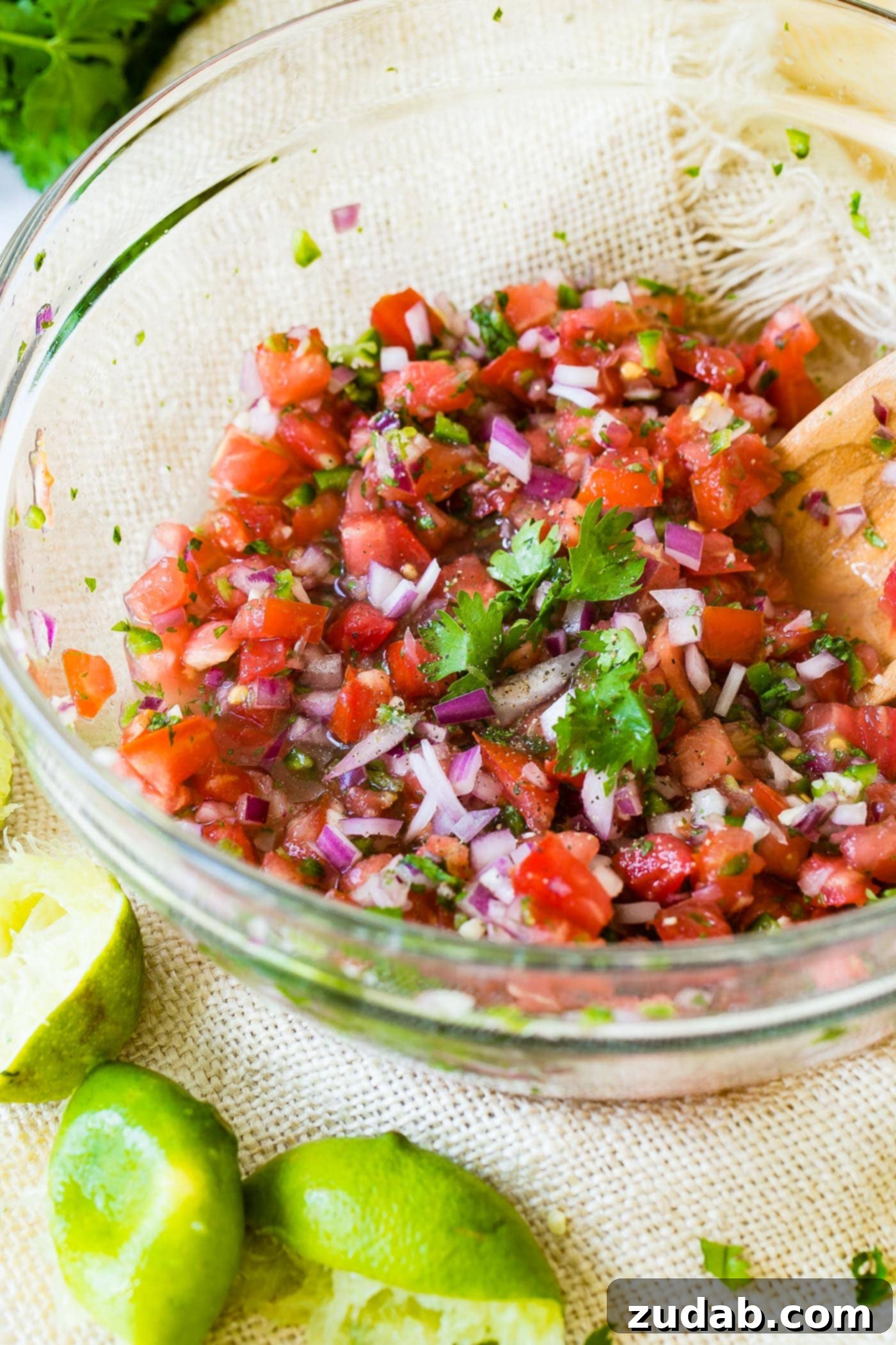 Stirring Homemade Pico de Gallo A glass bowl of vibrant Pico de Gallo being gently stirred with a wooden spoon, ready for serving.
