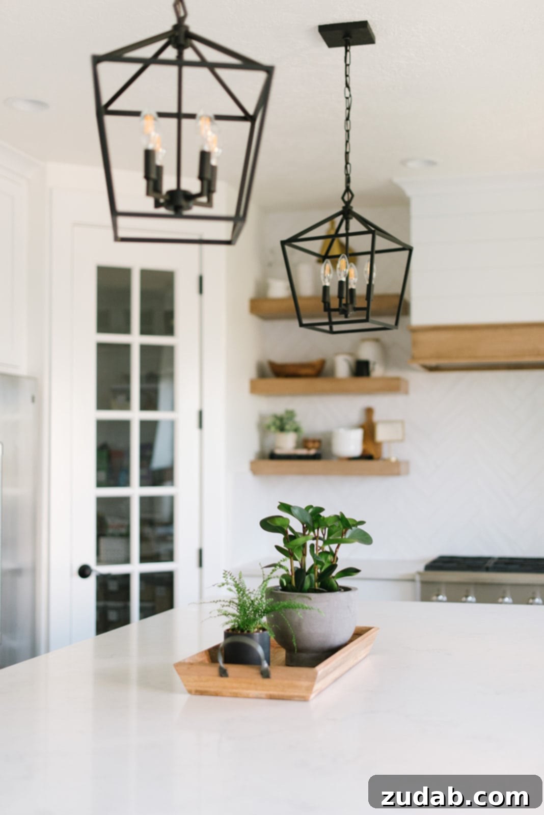 Contemporary all-white kitchen renovation showcasing a large island, crisp white cabinetry, artistic black lantern lights, and warm wood floating shelves