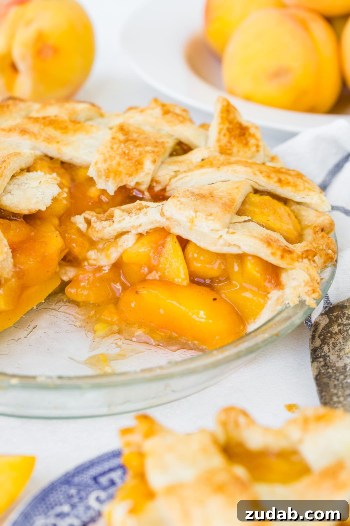 Fresh Peach Pie with Lattice Crust A photo of a fresh peach pie with a couple of slices missing and one slice ready to serve.