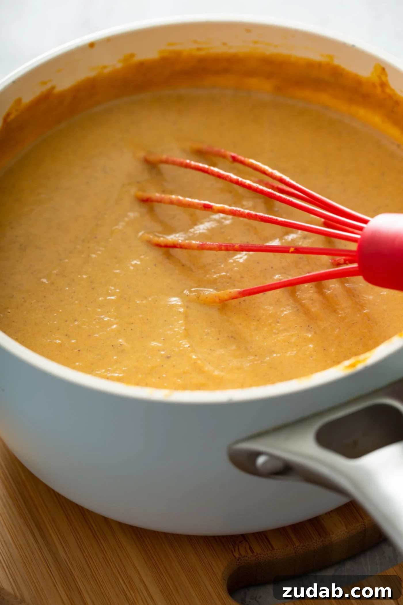 The Creamiest Pumpkin Ice Cream A medium sauce pan with pumpkin, spices and milk that has been whisked together with a red whisk.