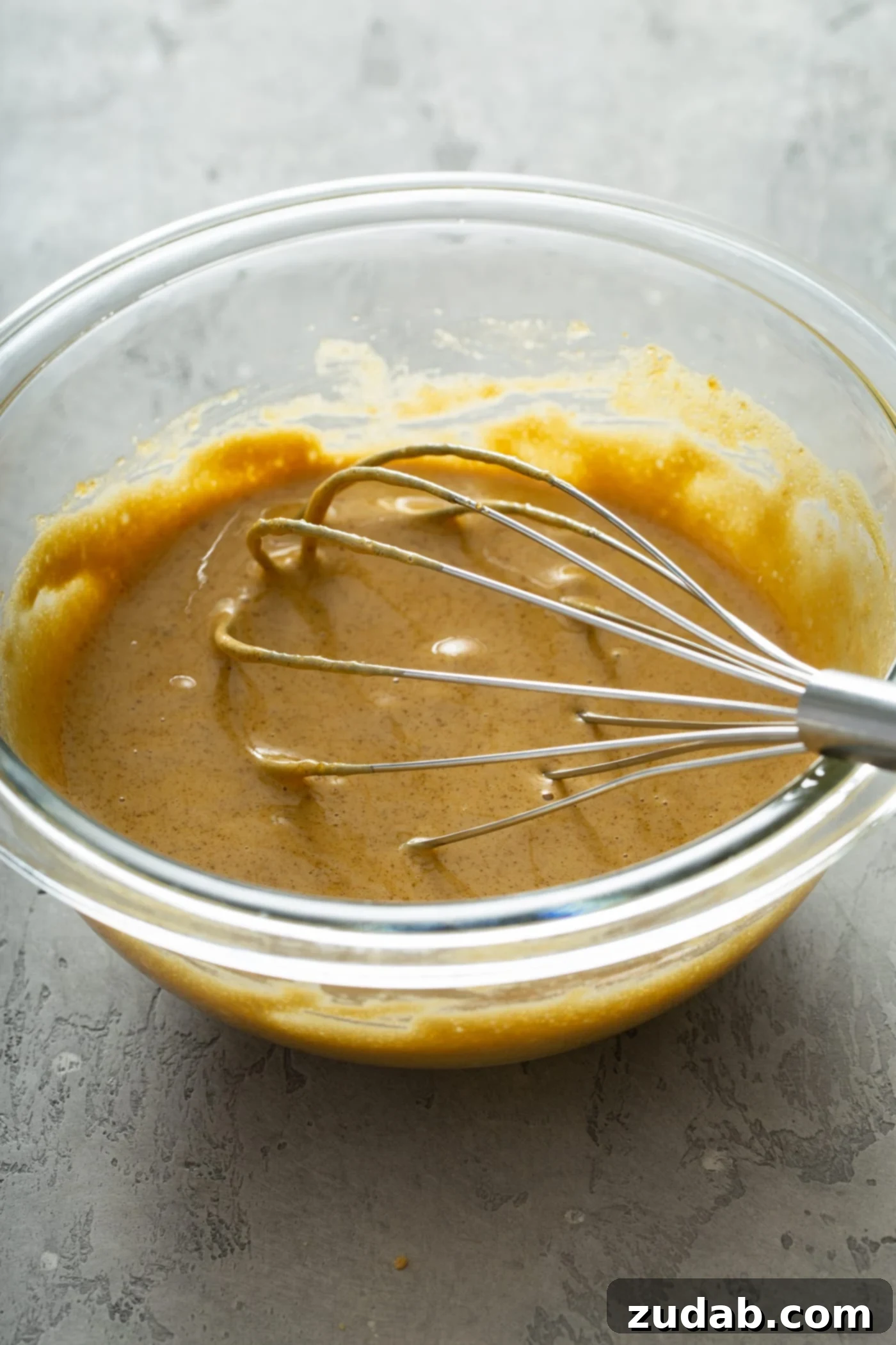 The Creamiest Pumpkin Ice Cream A glass mixing bowl with a whisk and brown sugar and egg yolks that have been whisked together.