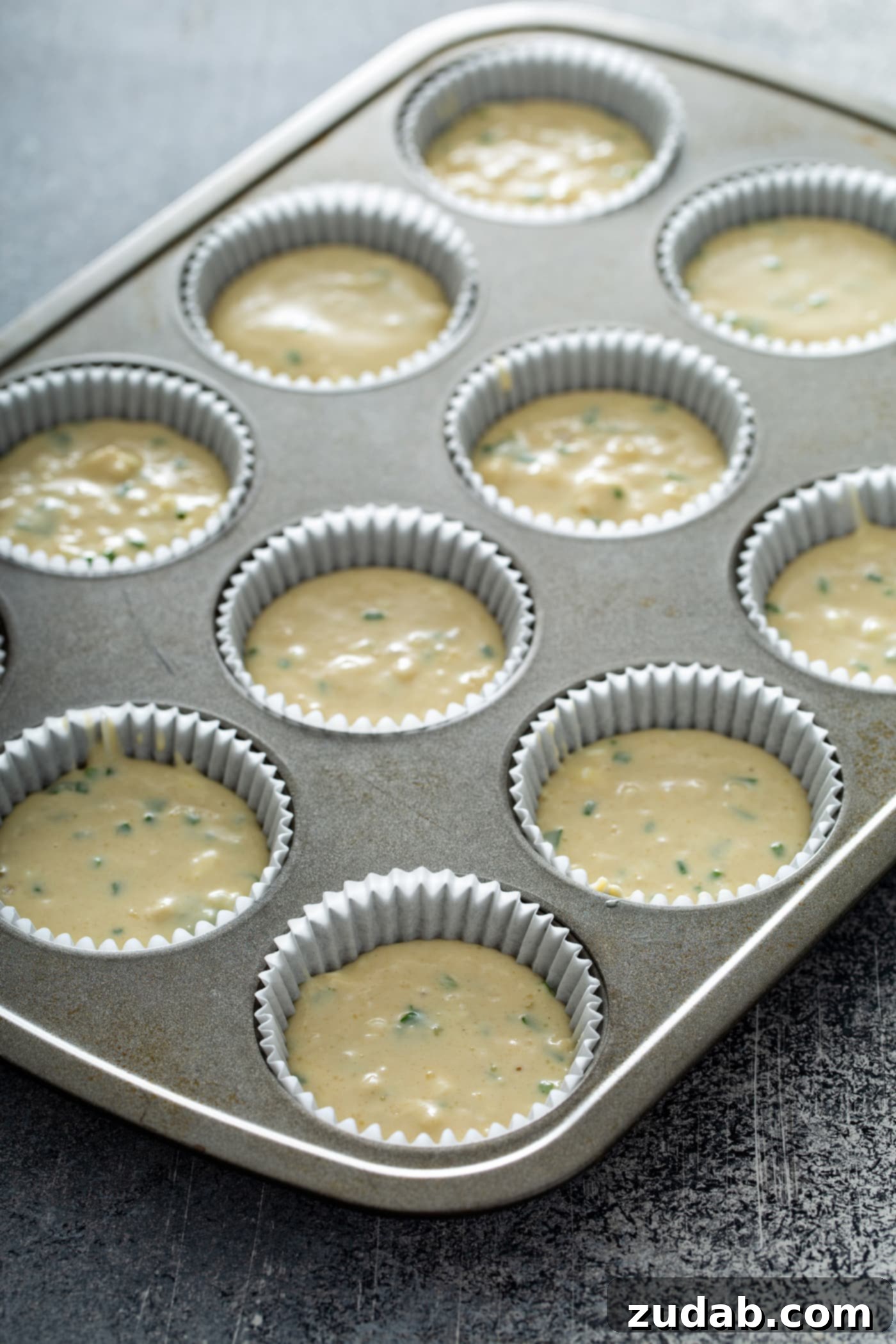 Quick and Easy Feta Muffins A muffin tin with muffin batter in white paper muffin liners.