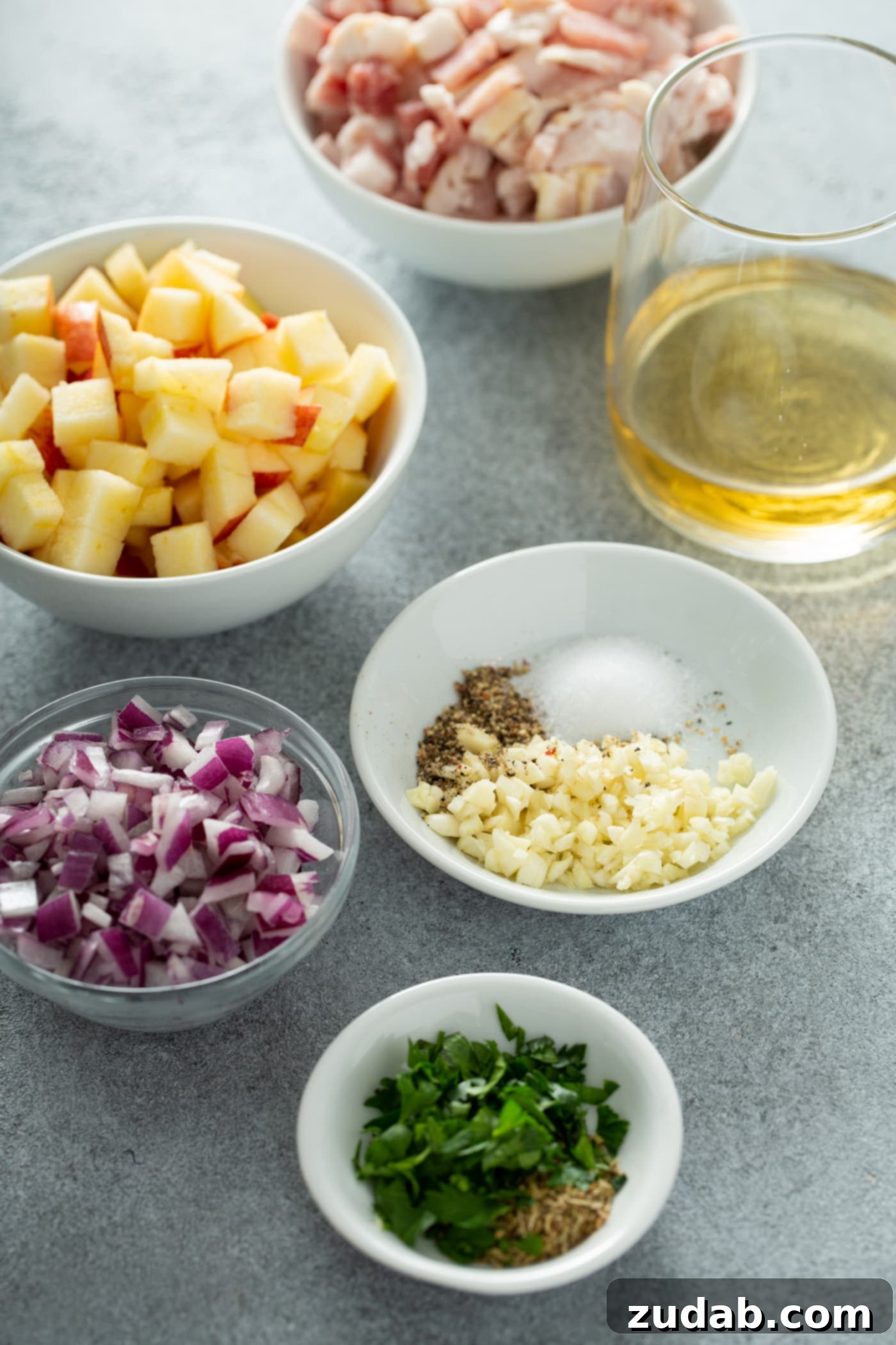 Maple Mustard Apple Chicken Burgers Five small bowls showcasing the prepared ingredients for the chicken burgers: perfectly cubed apples, finely chopped red onions, a mix of minced garlic with salt and pepper, a measure of clear apple juice, and a blend of vibrant minced parsley and fragrant sage.