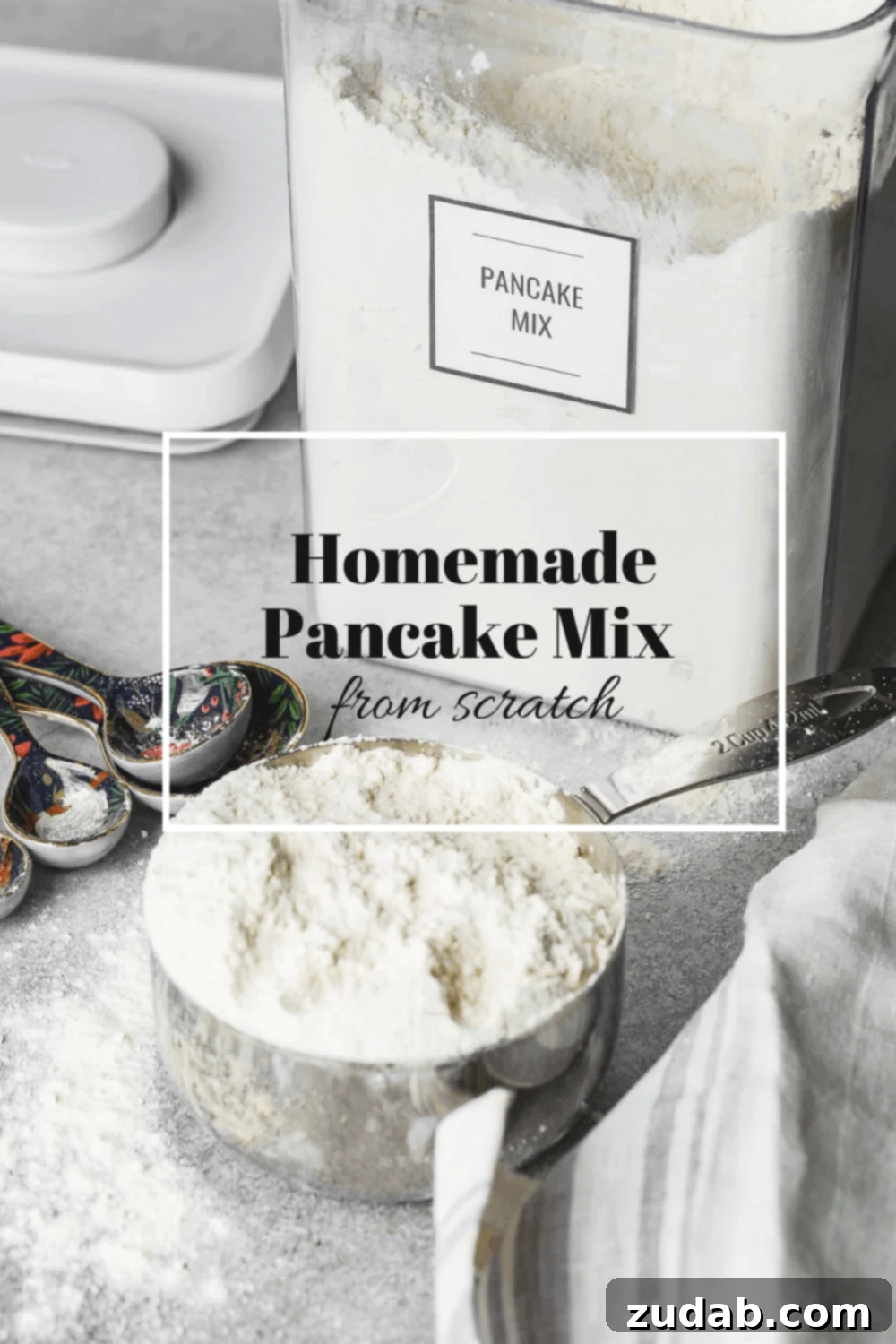 Easy Homemade Pancake Mix Recipe 6 A heaping cup of flour with metal measuring spoons laying on the table beside it. There is an open canister of flour in the background.