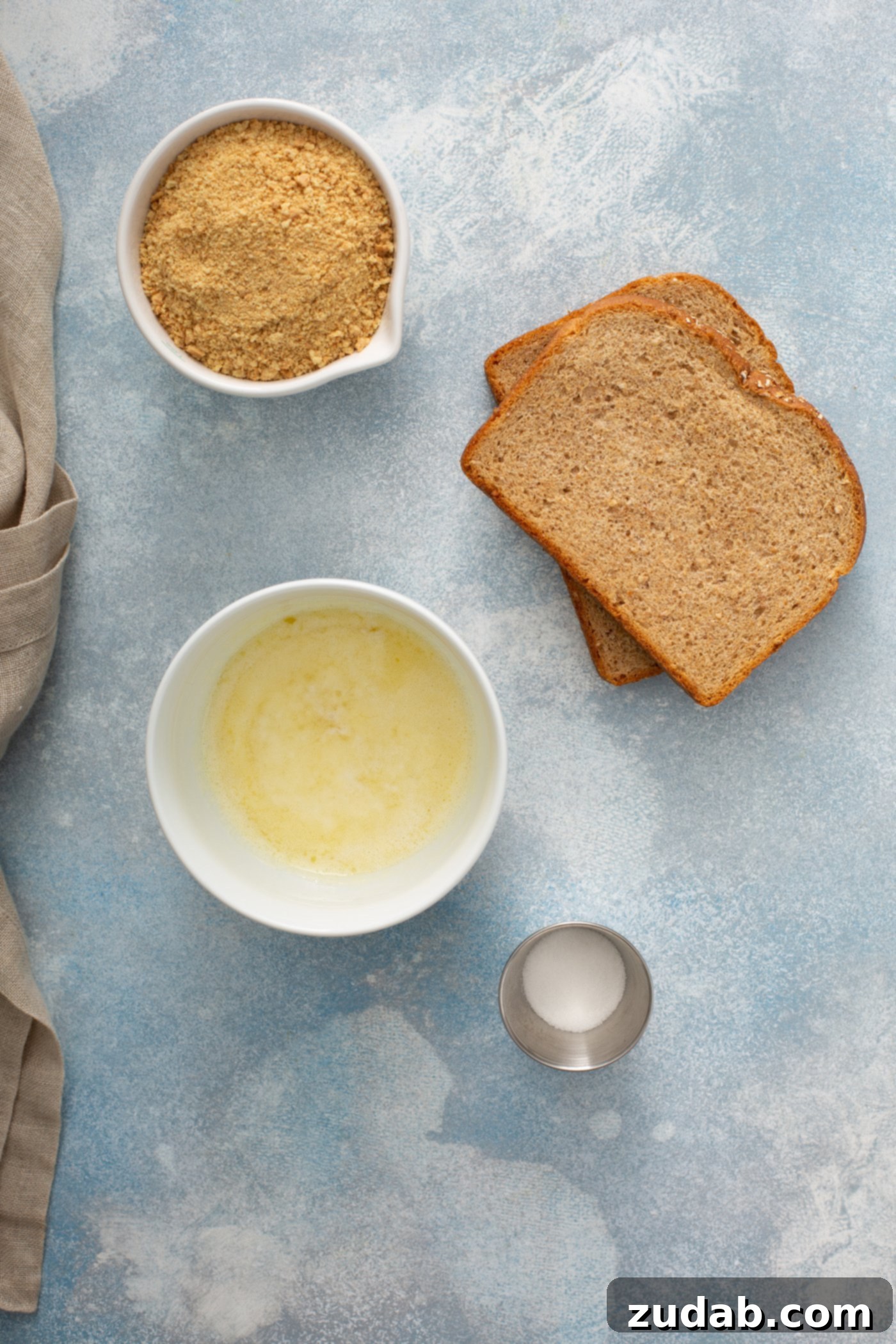 Apple Brown Betty Two slices of brown bread, with containers of melted butter, salt, cinnamon, and sugar laid out on a table, ready for preparing the Apple Brown Betty topping.